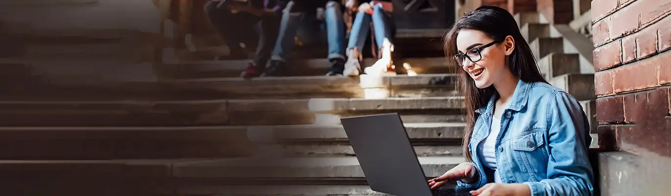 A SAP BTP student browsing laptop with happy face in college campus 