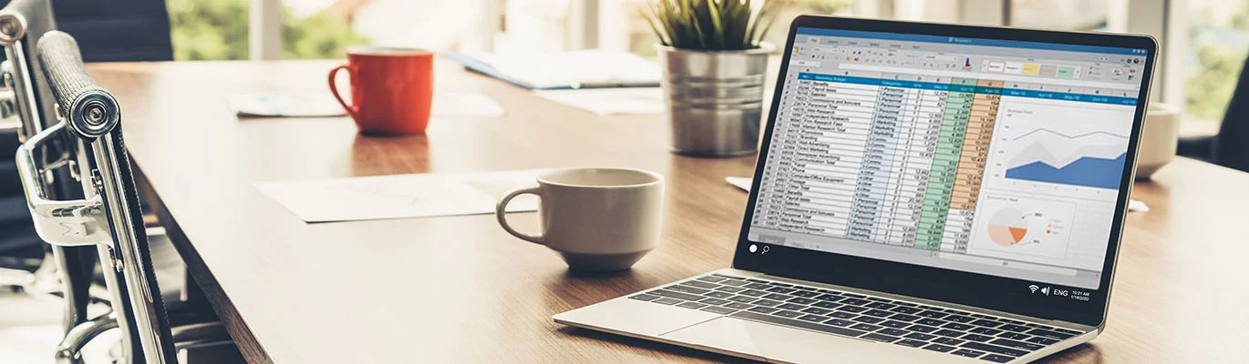 A Laptop displaying some reports in excel sheet placed on a table with a tea cup nearby