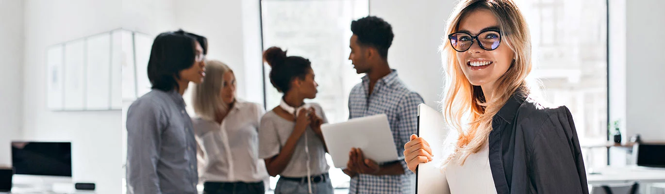 An app developer standing with a laptop while other four colleagues having a discussion behind 