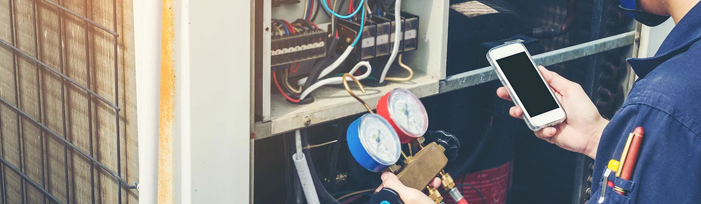 Hand of a HVAC professional holding a mobile phone and a gauge