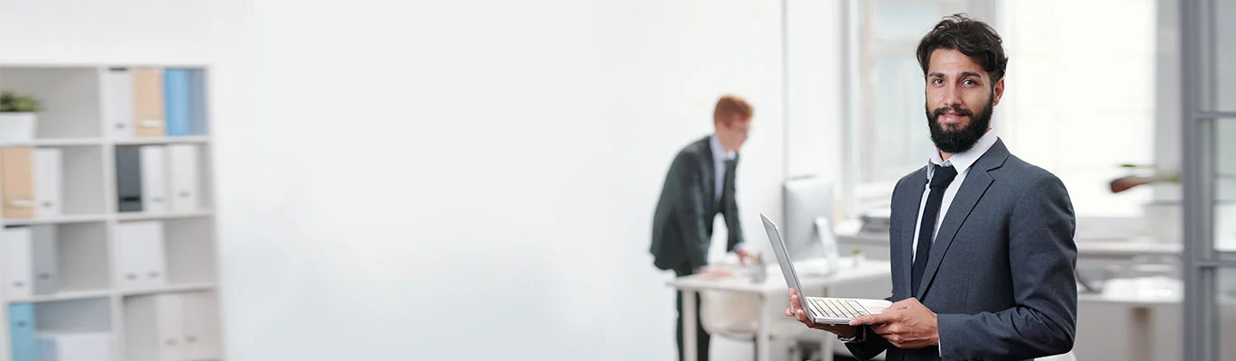 A Jewellery designer standing with a laptop at work place while other designer working behind