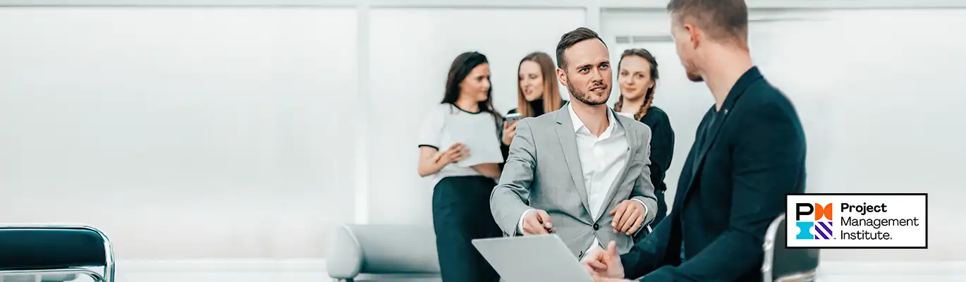 Two project managers having a discussion standing infront of a laptop while other three colleagues standing behind them 