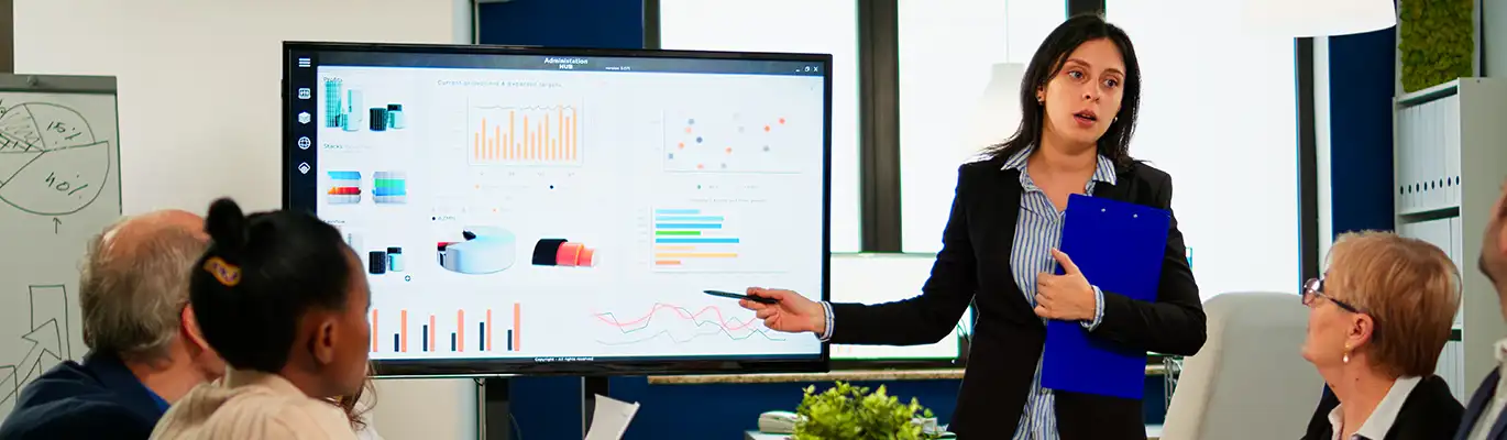 A facilities manager educating her team pointing out the graph shown on projector screen while team members are sitting infront of her