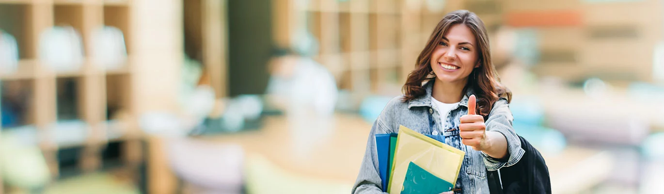 An English speaking course student with a shoulder bag and some books in one hand showing thumbs up 