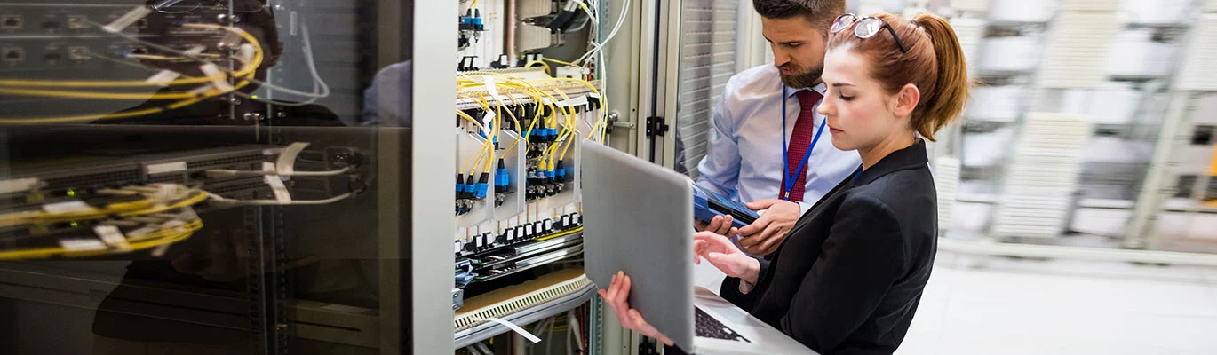 Two network professionals can be seen working in a cable room.