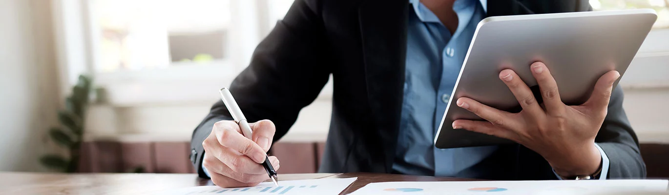 A hand holding a tablet and noting down something from it 