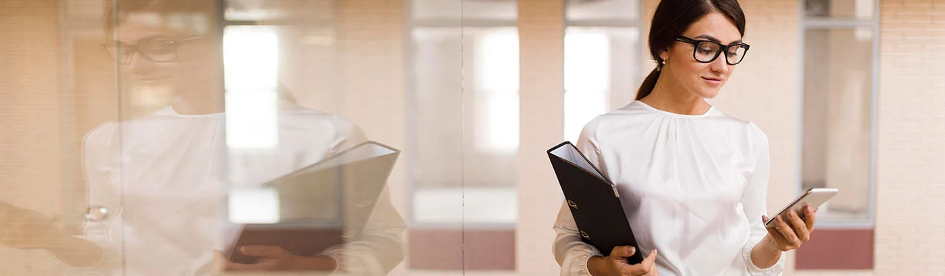 Photo of an office secretary holding files and checking her phone. 