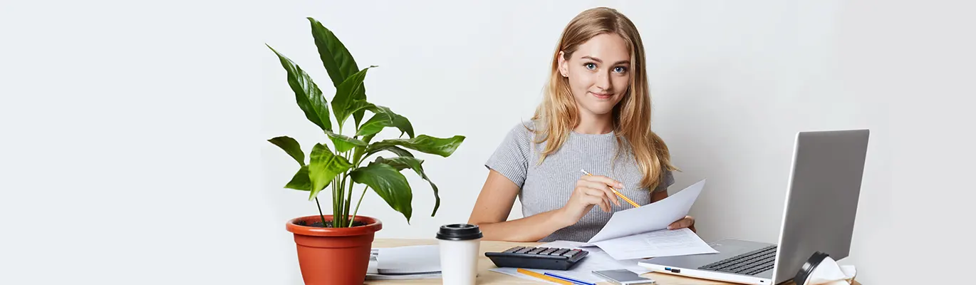 Business Report writing professional sitting infront of a laptop and holding paper on hand