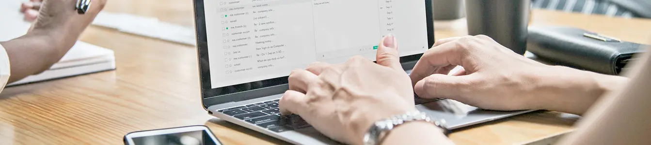 Hands of a IT professional typing on a laptop with a mobile phone near by