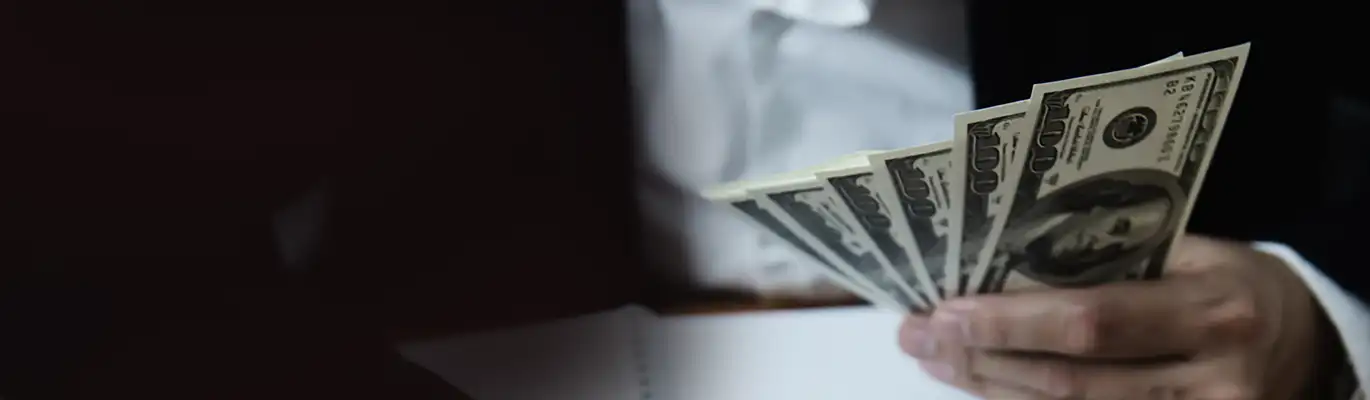 A hand holding six currency notes in a dark background