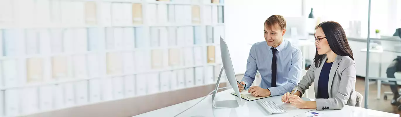 Two professionals sitting infront of a computer, having discussion looking on the screen 