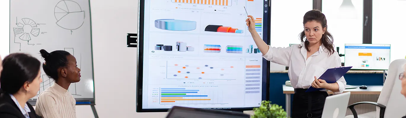 A leader holding notepad and educating her team by showing project on screen