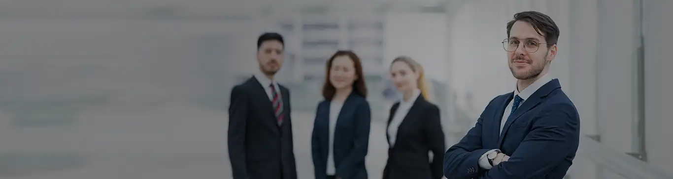 A professional man standing with holded hands while other three professionals standing behind him. All looking to the camera. 