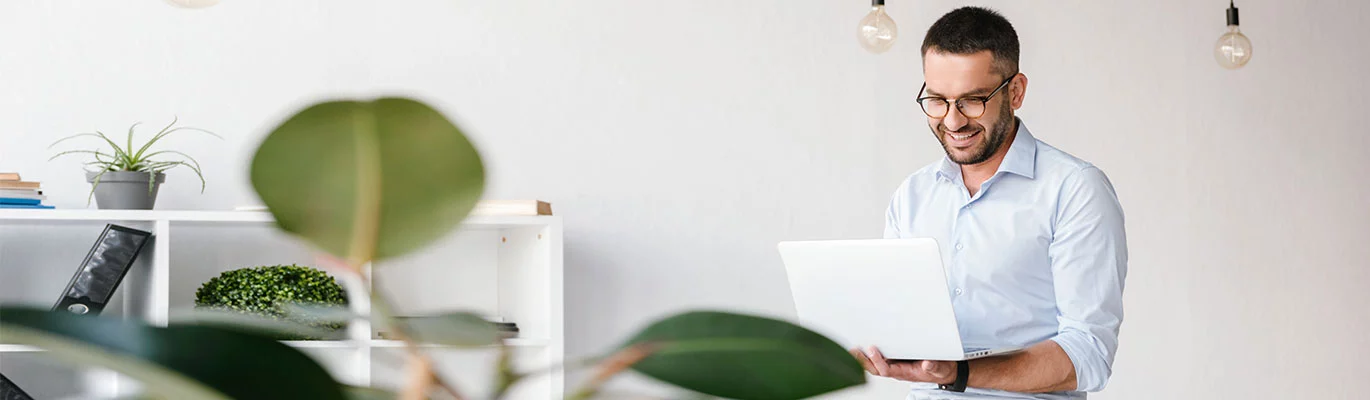 An IT professional looking to the laptop holding in hand with a smiling face