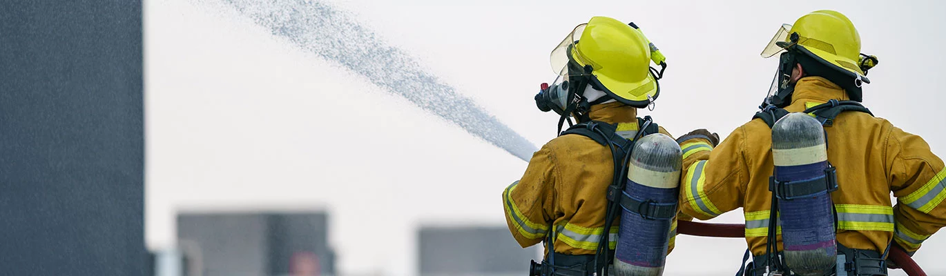 Two firefighters standing together and pumping water to a nearby building