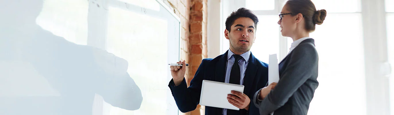 A Team leader standing infront of a white board giving Presentation Skills Training to a female team member