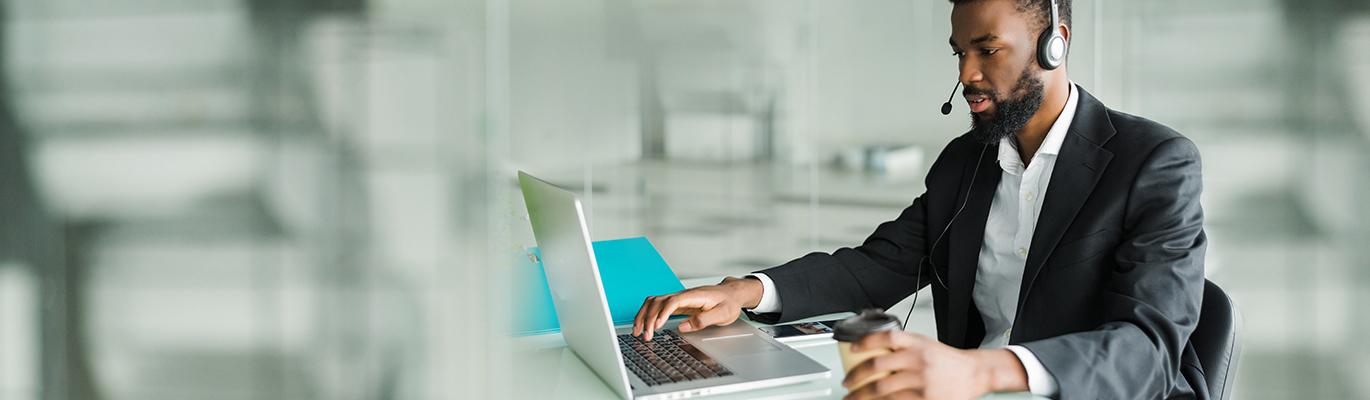 A cloud computing professional wearing a headphone with mic is working on a laptop