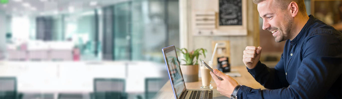 CIMA professional sitting in front of a laptop holding a phone victory smiling