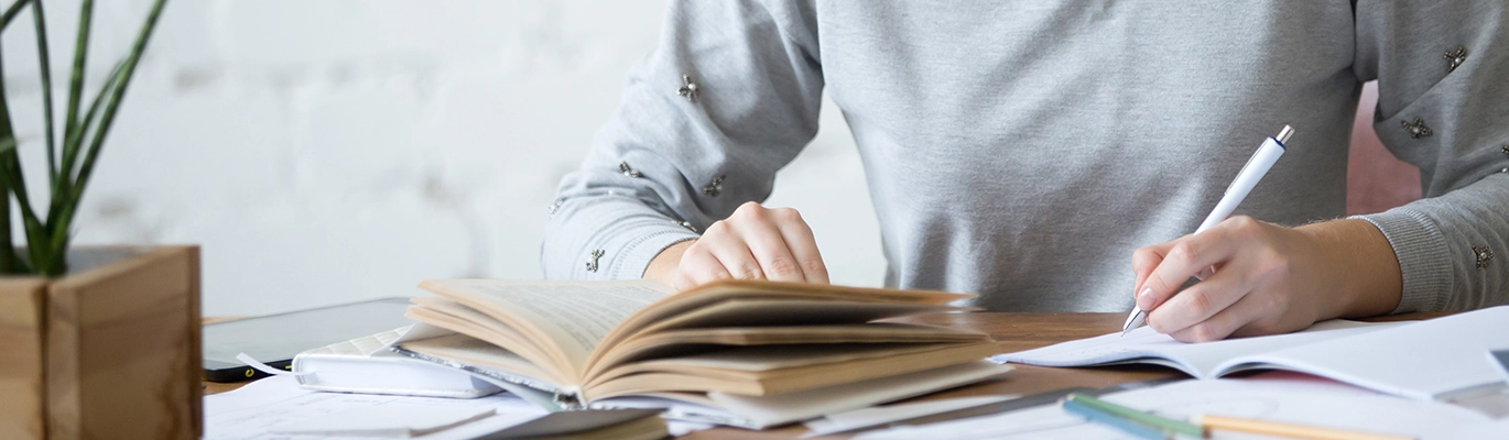 A student referring a textbook and writing on a notebook