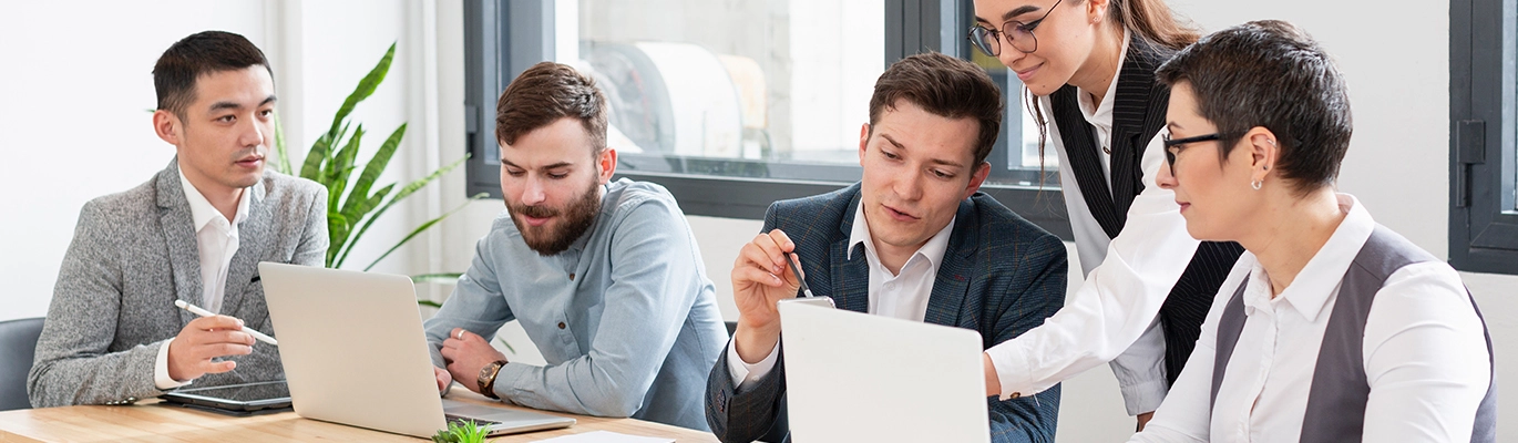 Five professionals interacting with each other and working on laptops