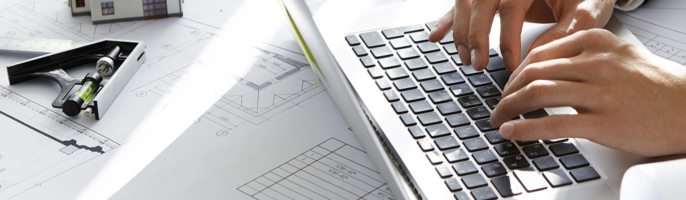 A person typing on a laptop surrounded by structural design tools