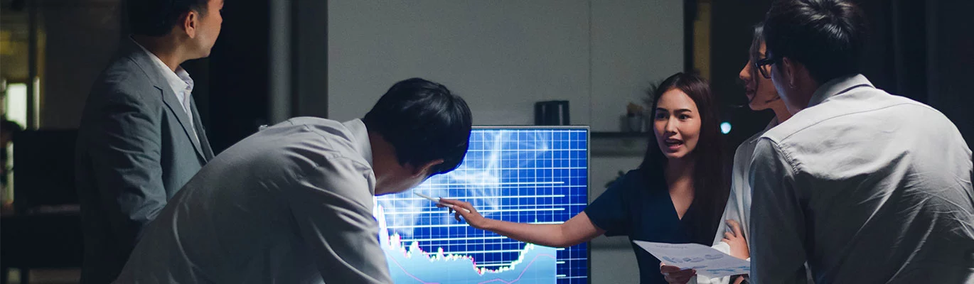 Five MS PowerPoint professionals on a group discussion with a computer displaying a graph, one of them pointing towards the screen